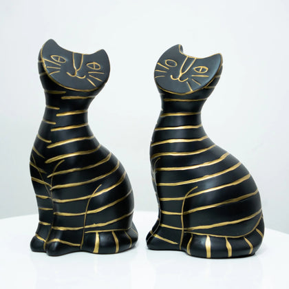 Two black cat figurines with gold stripes and gold line details on their faces, displayed side by side on a white surface against a white background.