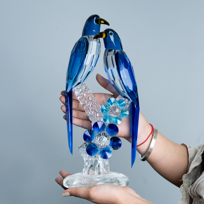 A blue and clear crystal bird figurine displayed on a person's hands against a plain light gray background.