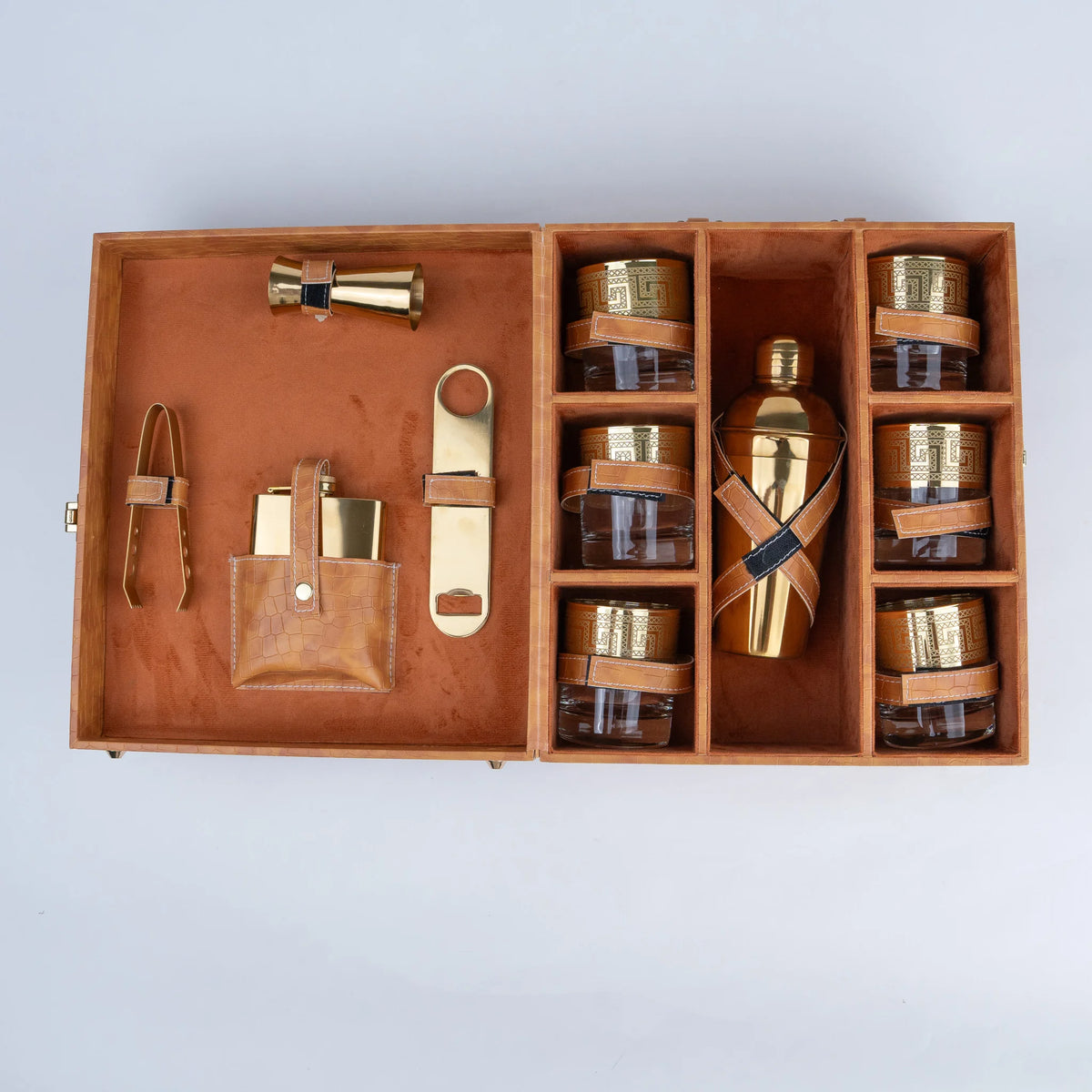 A luxury bar gift set in a wooden presentation box, featuring a gold-toned bottle with a leather wrap, six small amber glass jars with gold lids, a leather pouch with gold accessories, and a brass tongs, all arranged neatly inside an open light brown leather.