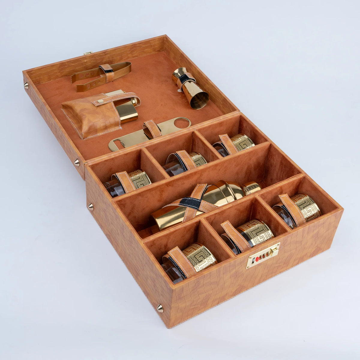 A wooden presentation box with multiple compartments, shown open. Inside are several small bottles with gold-toned caps and leather loops, plus a folded leather pouch and a brass-toned tool or accessory.