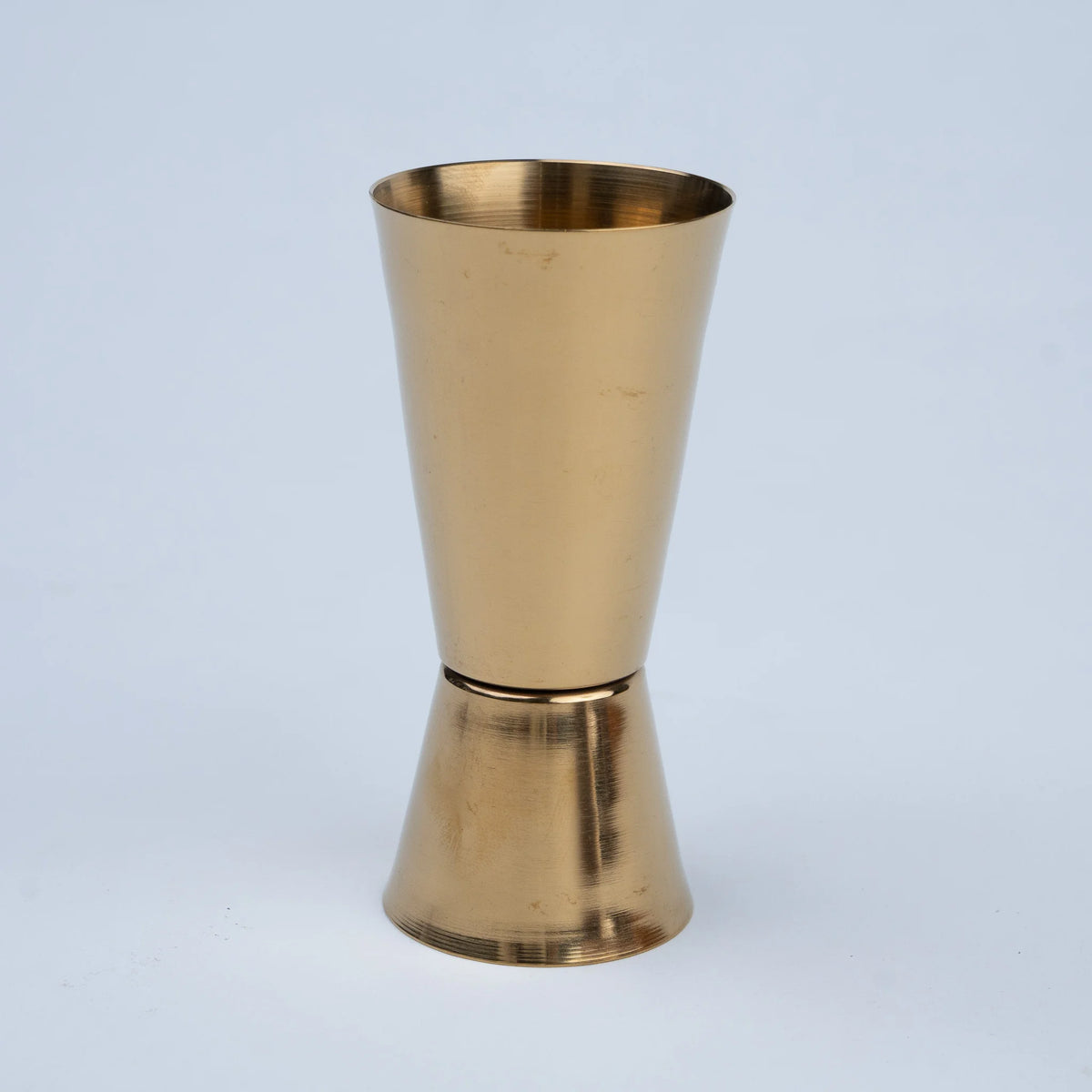 A double-sided jigger with a brushed brass finish, standing upright.