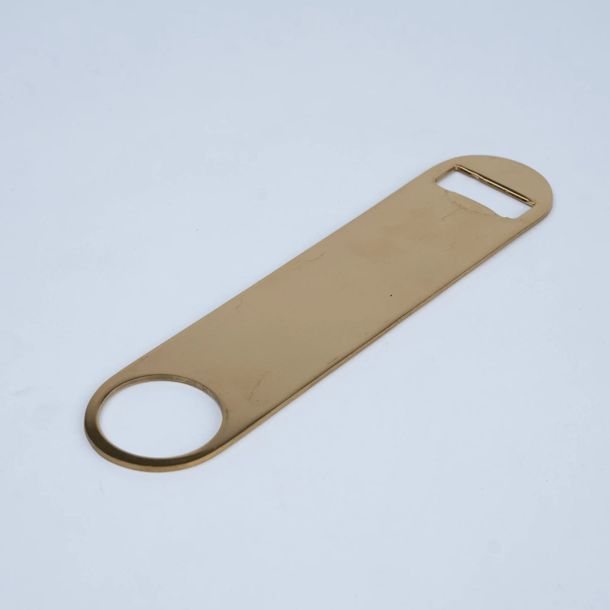 A gold-colored metal bottle opener with a circular pull tab and a flat blade.