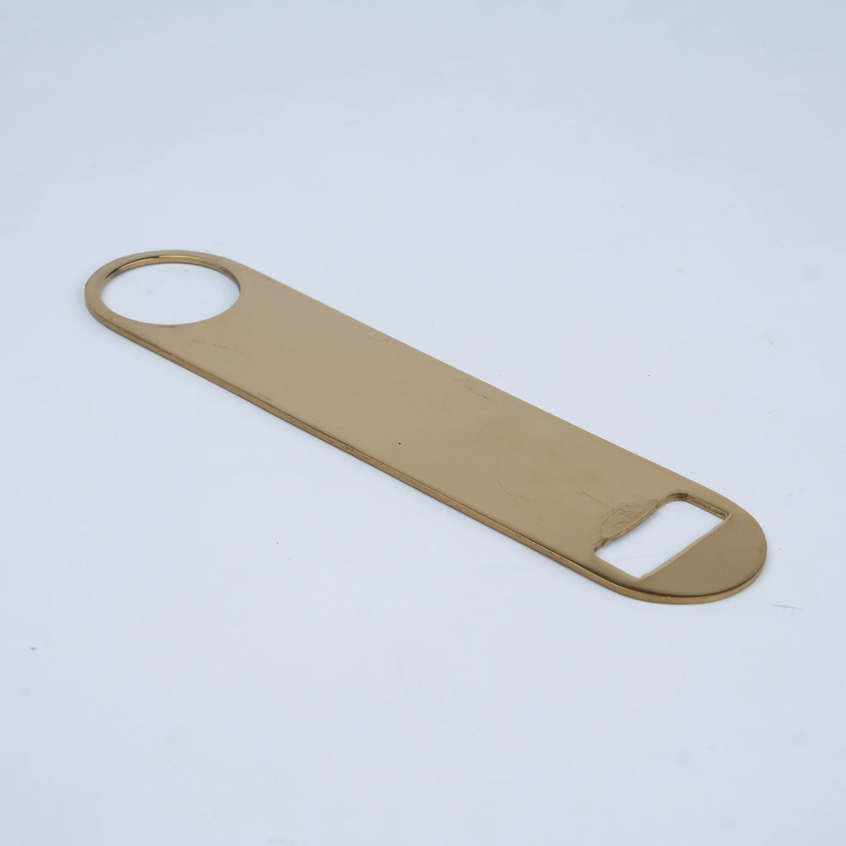 A flat, rectangular bottle opener with rounded corners in a warm gold or brass finish,