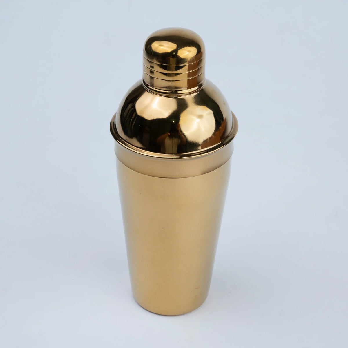 A polished gold metal cocktail shaker with a matching lid.