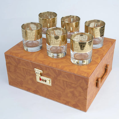 A set of six gold-patterned glass tumblers arranged on top of a brown wood-grain storage box with a gold combination lock and handle