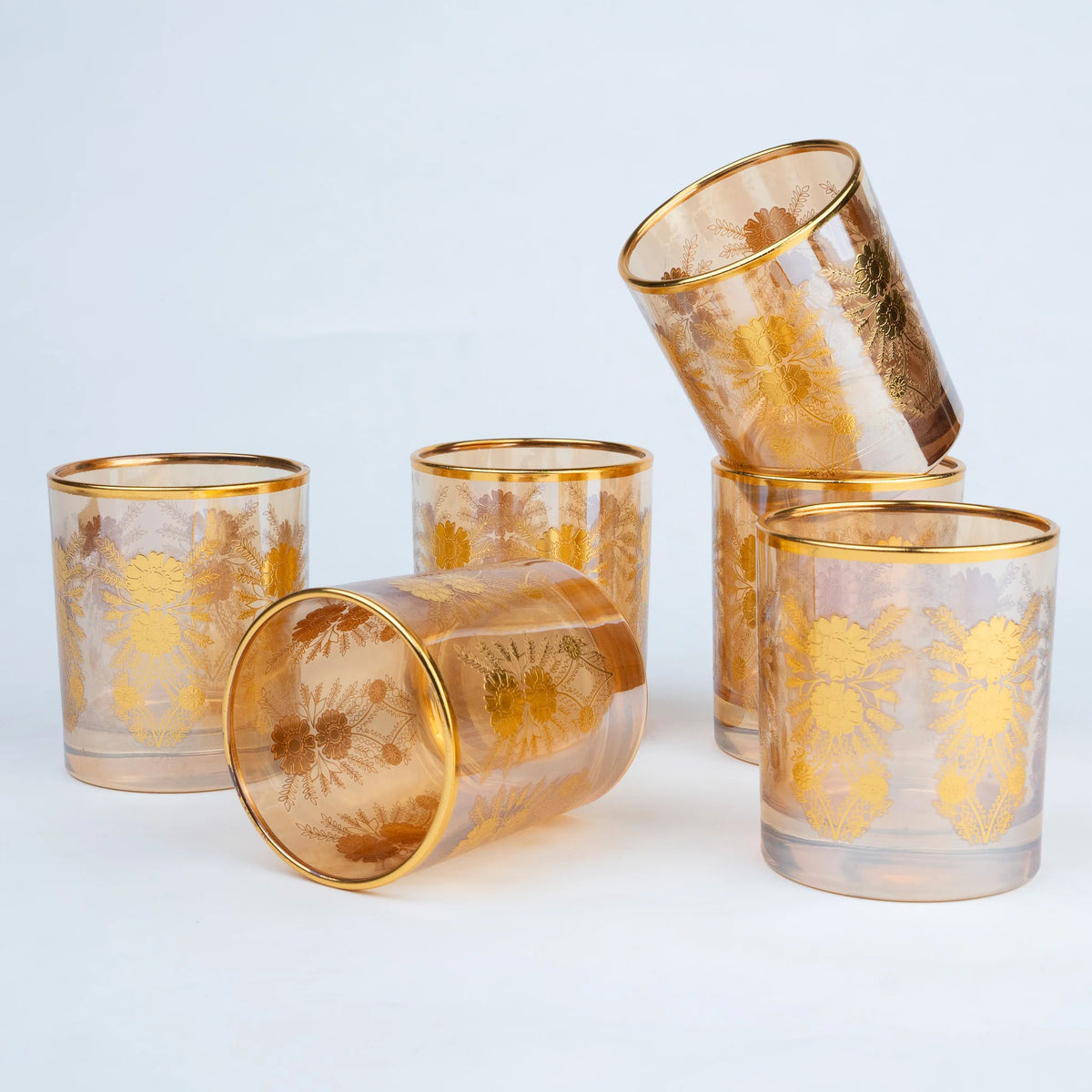 Five amber-tinted glass tumblers with gold floral patterns and gold rims.