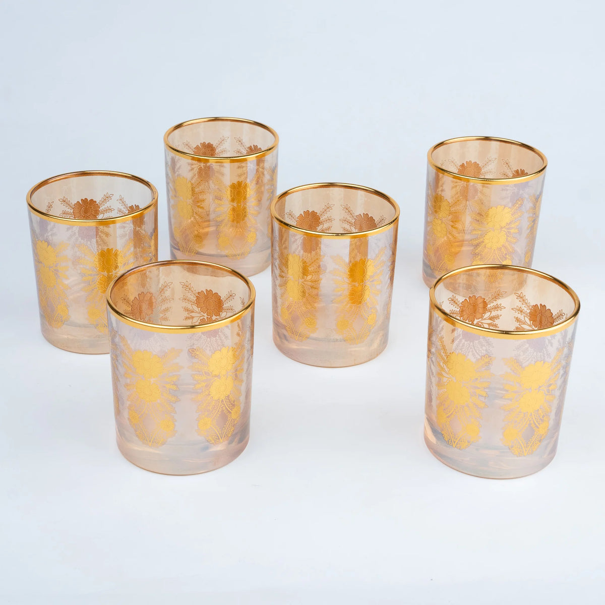 Six clear glass tumblers with gold rims and gold floral patterns.