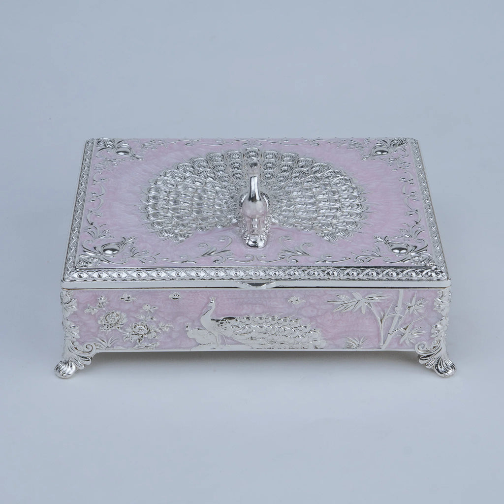 A decorative silver jewelry box with a light pink enamel or lacquer base, featuring embossed peacock and floral motifs, ornate silver scrollwork borders, and small silver feet.