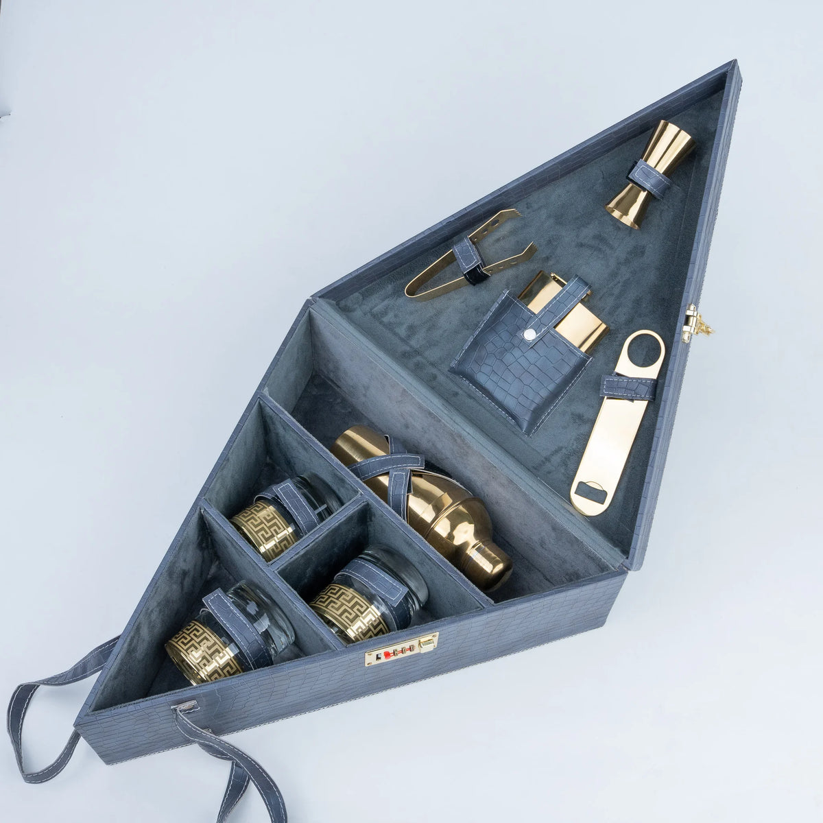 A dark gray wooden cocktail gift set organizer shown open, containing gold-toned metal bar tools and bottles with dark blue leather straps.