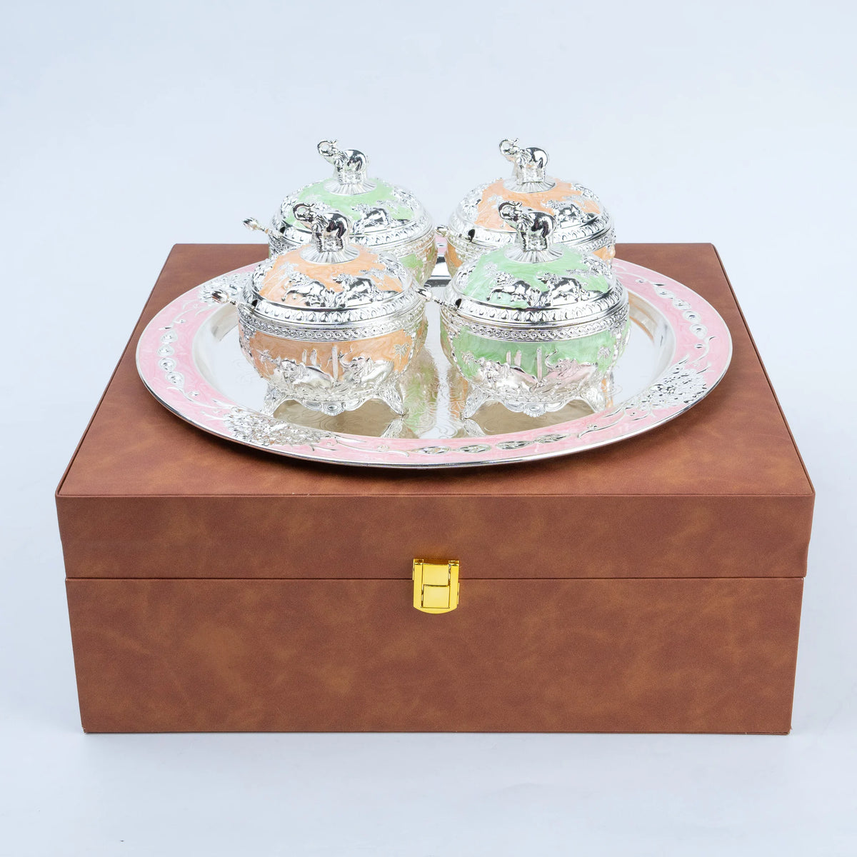 A set of four decorative sugar bowls with silver lids and pastel-colored interiors, presented on a round silver tray atop a brown box with a gold clasp.