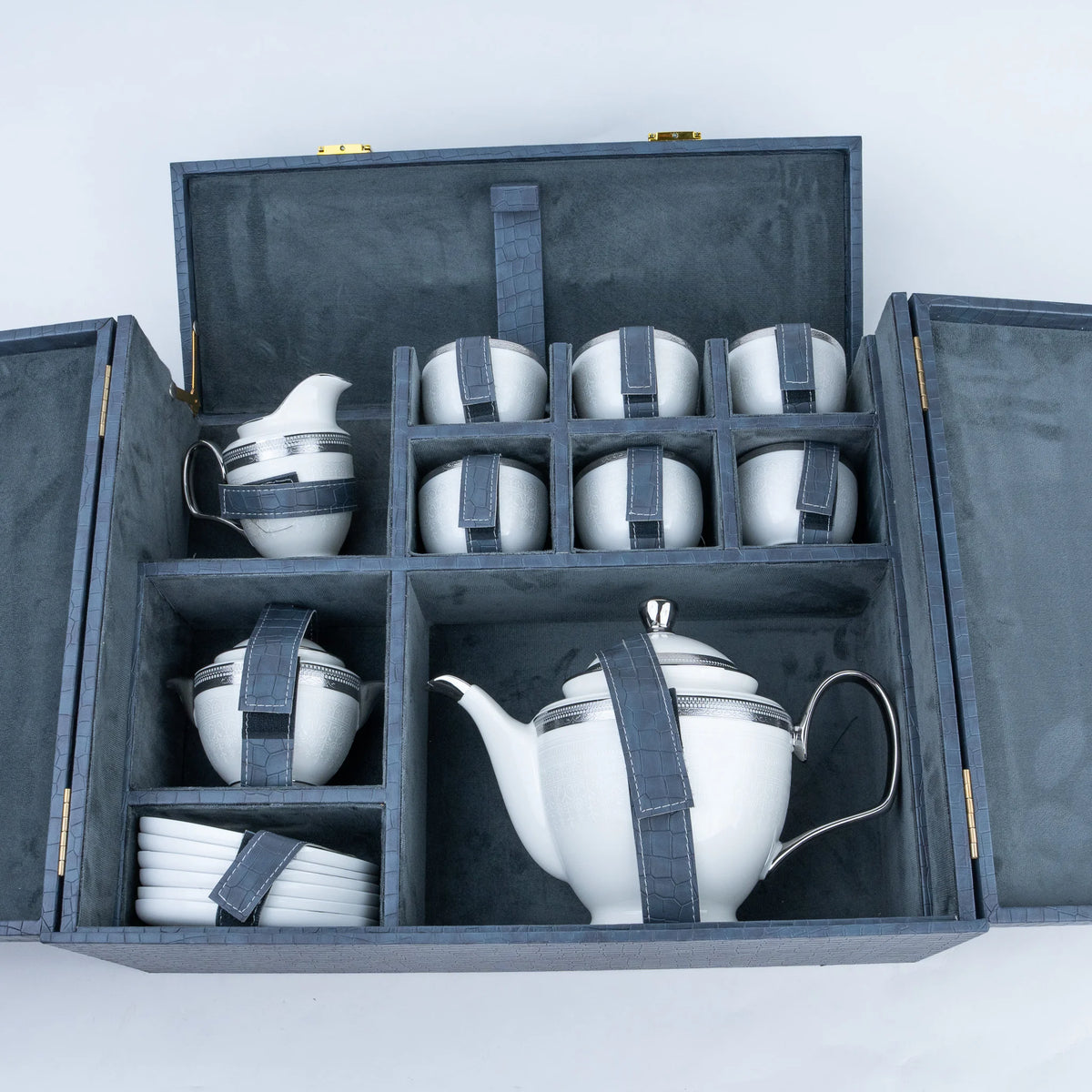 White ceramic tea and coffee set with matching cups, saucers, and a teapot, each wrapped in a dark gray fabric strap, displayed inside an open dark gray presentation box.