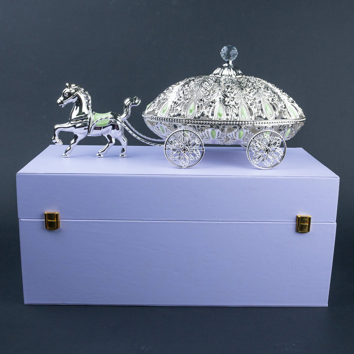 A silver horse-drawn carriage ornament or decorative piece displayed on top of a lavender gift box 