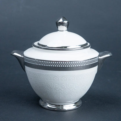 A white ceramic lidded sugar bowl or creamer with silver-toned metal handles, spout, lid knob, and decorative bands, photographed on a dark gray studio background.