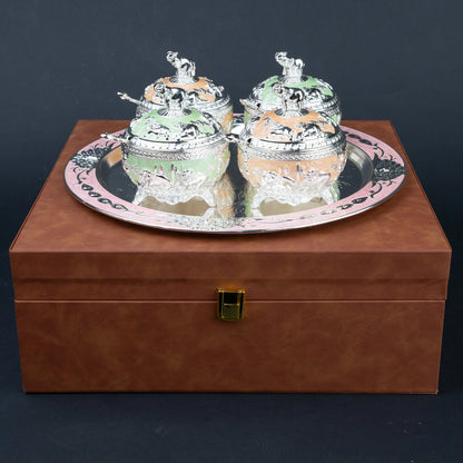 A pair of ornate silver-toned decorative boxes with colorful pastel inserts, displayed on a round silver tray atop a brown presentation box.