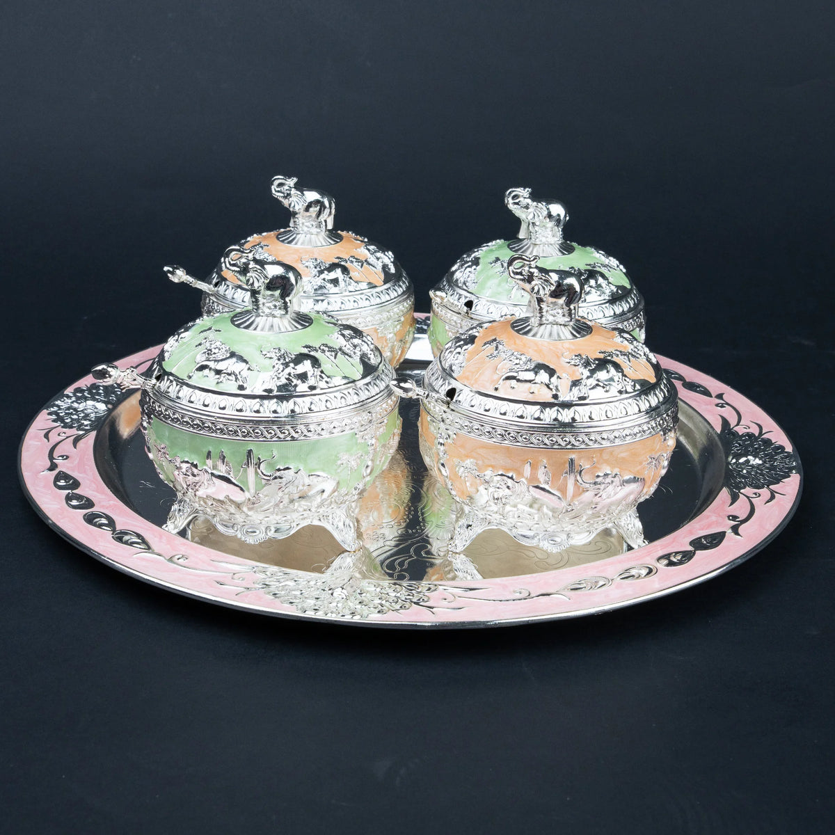 Four elephant lidded decorative containers in mint green and peach arranged on ornate silver tray