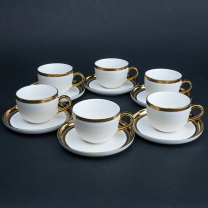 Six white ceramic teacups with gold trim and matching saucers arranged on a dark charcoal background.