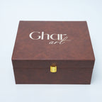 A rectangular brown textured box with a gold clasp and the words 'Ghar art' printed in white on the lid, photographed on a light gray background.