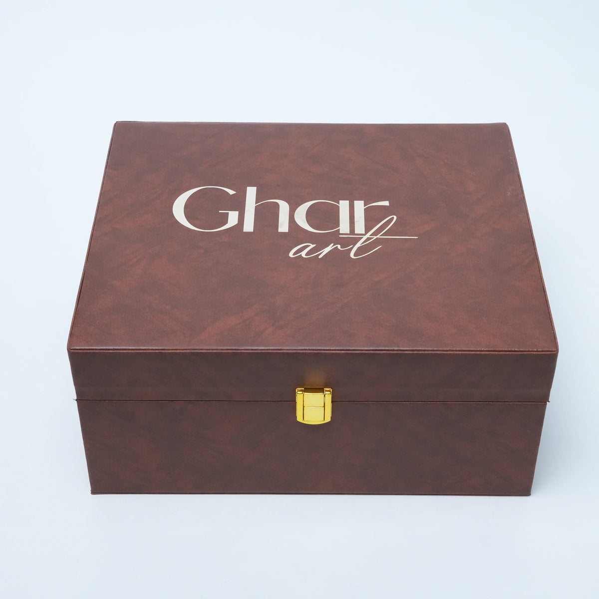 A rectangular brown textured box with a gold clasp and the words 'Ghar art' printed in white on the lid, photographed on a light gray background.