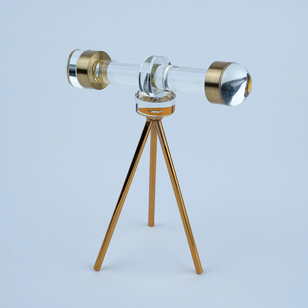 A clear glass or acrylic telescope-shaped object displayed on a small metallic tripod stand 