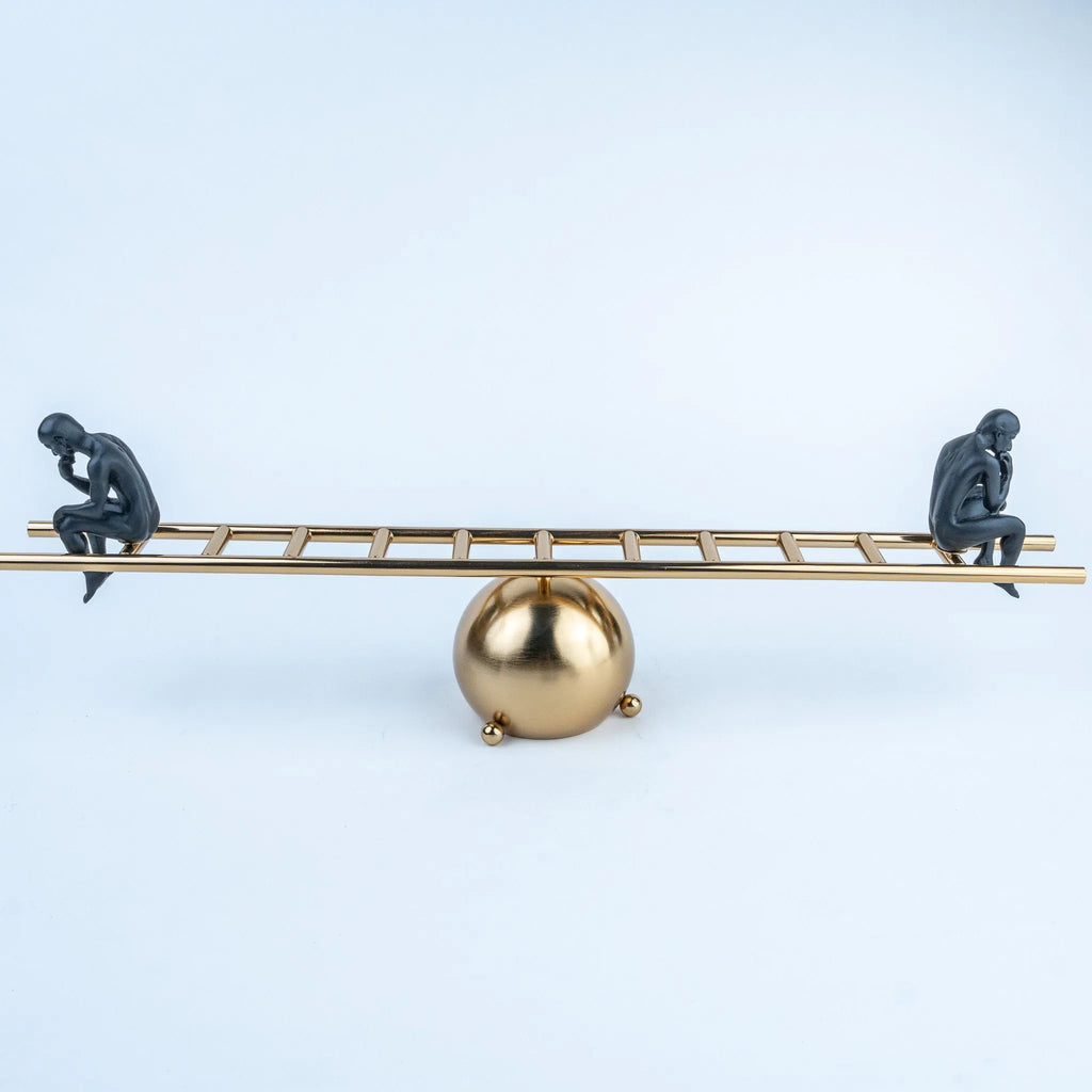 Gold ladder-inspired tabletop sculpture with two seated black human figures.