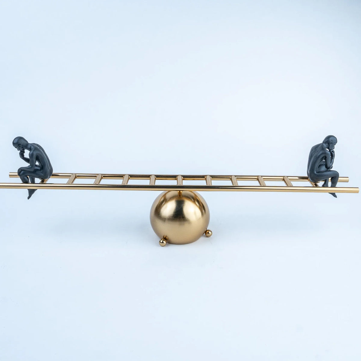 Gold ladder-inspired tabletop sculpture with two seated black human figures.