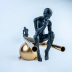 Two black contemplative figurines on a gold ladder-inspired decorative sculpture.
