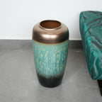 Decorative vase with bronze top and teal body on a gray floor.