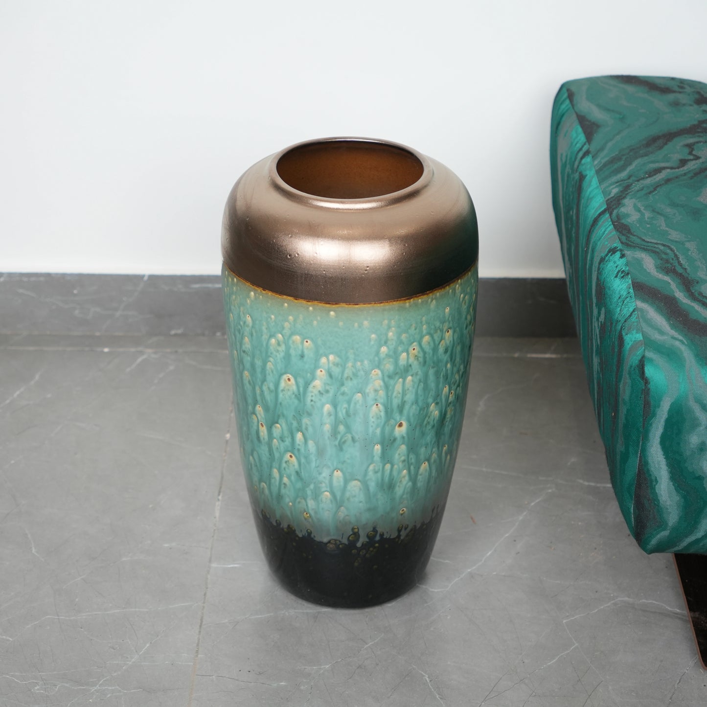 Decorative vase with bronze top and teal body on a gray floor.