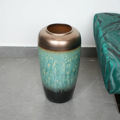Decorative vase with bronze top and teal body on a gray floor.