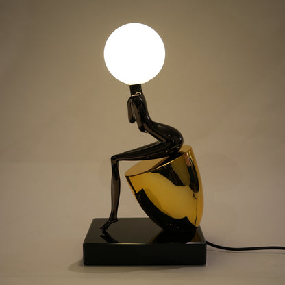 Modern table lamp with black and gold base and spherical white light bulb on a neutral background