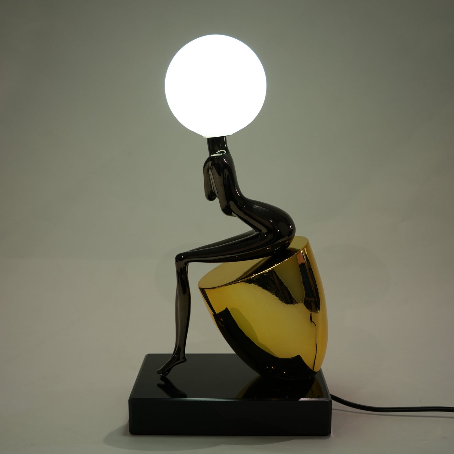 Black figure table lamp with glossy finish and spherical globe light mounted on a solid base
