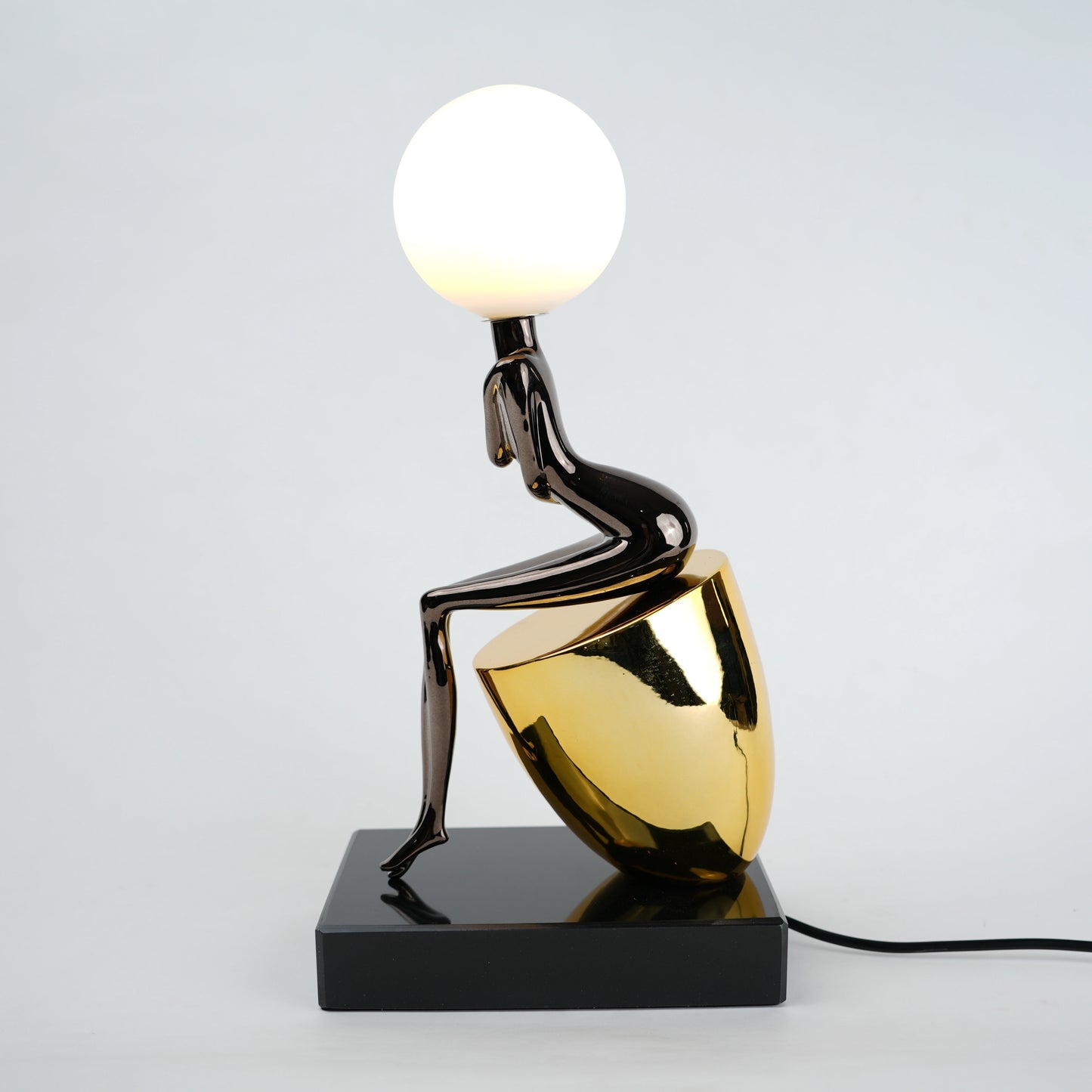 Black figure table lamp with glossy finish and spherical globe light mounted on a solid base