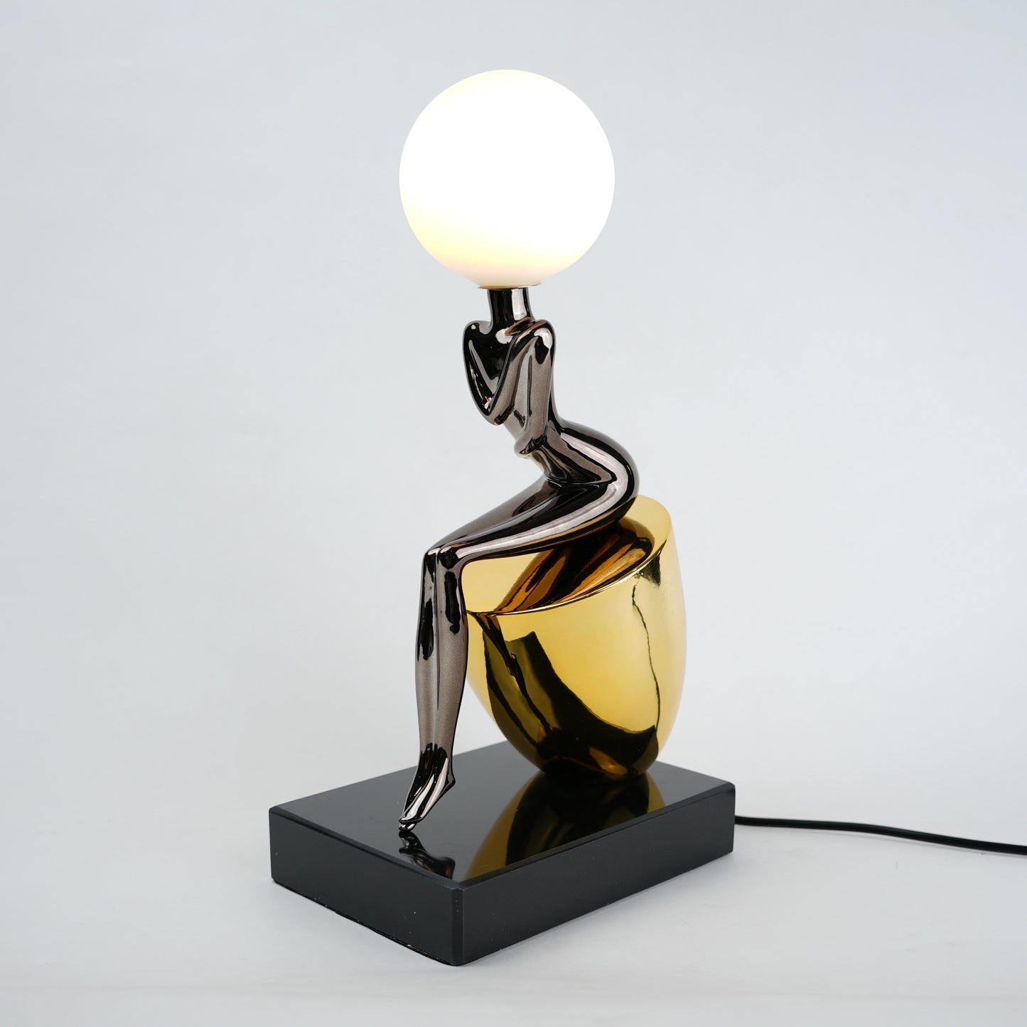 Black figure table lamp with glossy finish and spherical globe light mounted on a solid base