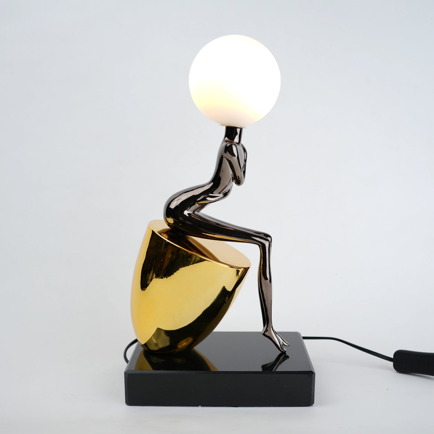 Black figure table lamp with glossy finish and spherical globe light mounted on a solid base