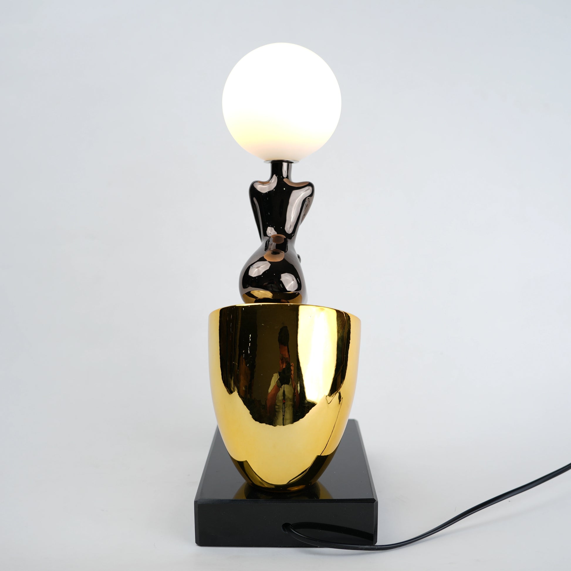 Black figure table lamp with glossy finish and spherical globe light mounted on a solid base