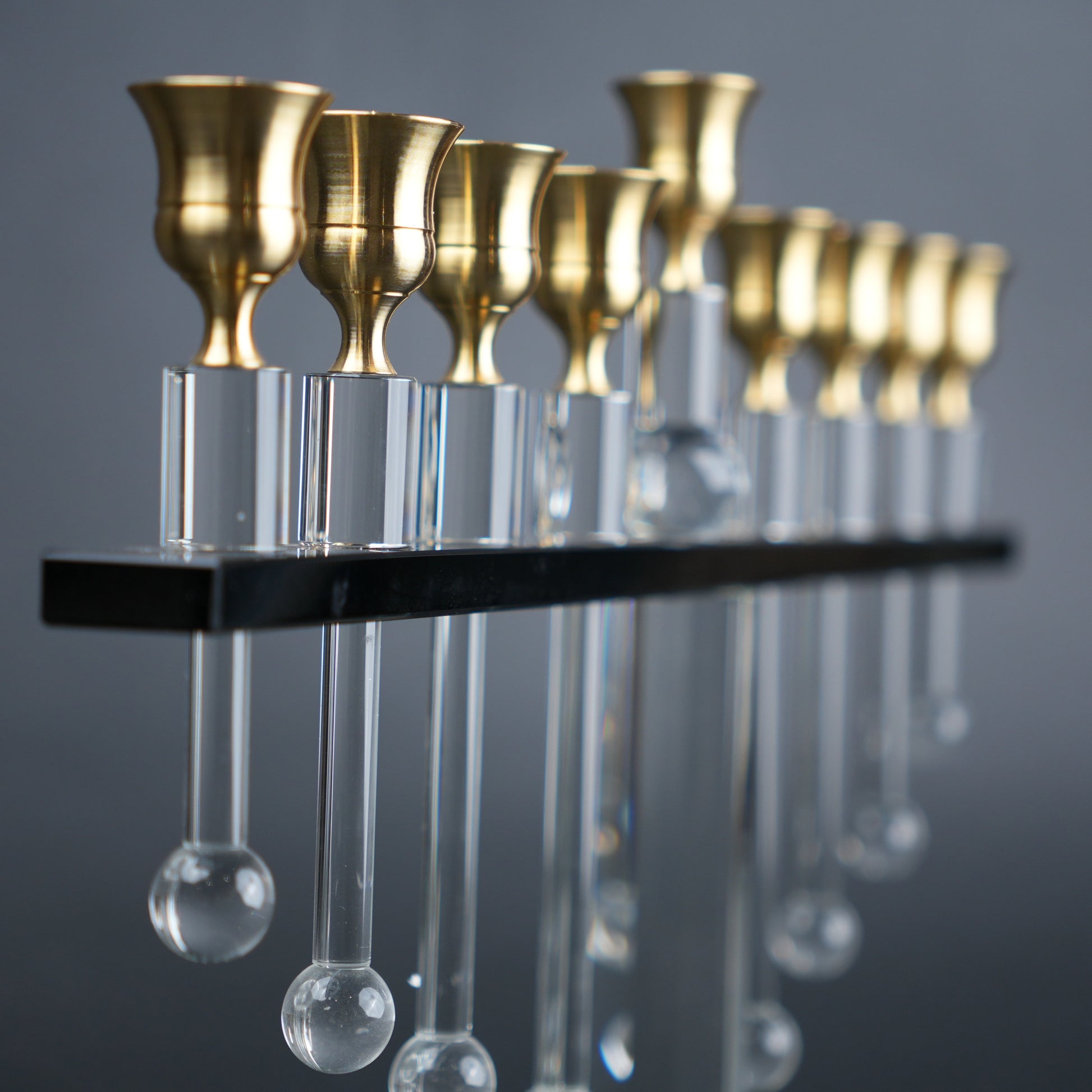 Decorative hanging fixture with gold candle holders and clear glass droplets on a gray background