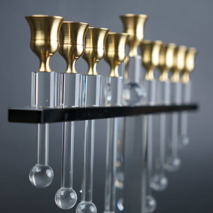 Decorative hanging fixture with gold candle holders and clear glass droplets on a gray background