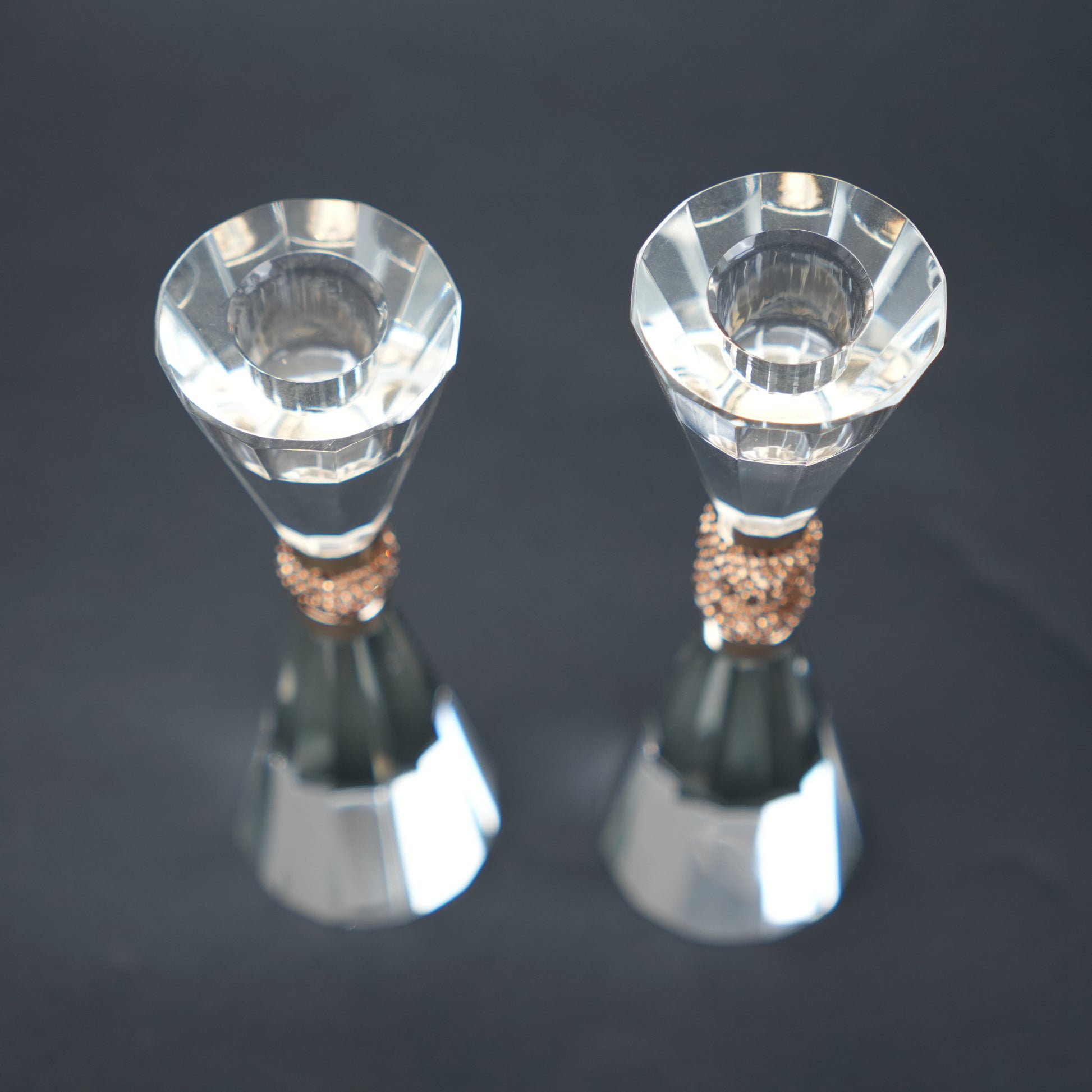 Two crystal candle holders with bronze bases on a dark background