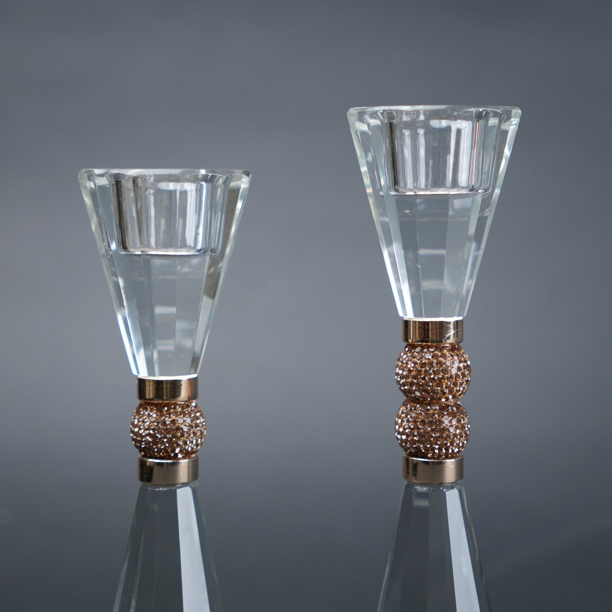 Two crystal candle holders with bronze bases on a reflective surface.