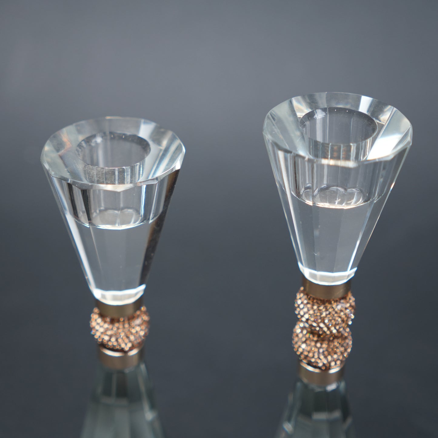 Two clear crystal candle holders with rose gold bases on a reflective surface.