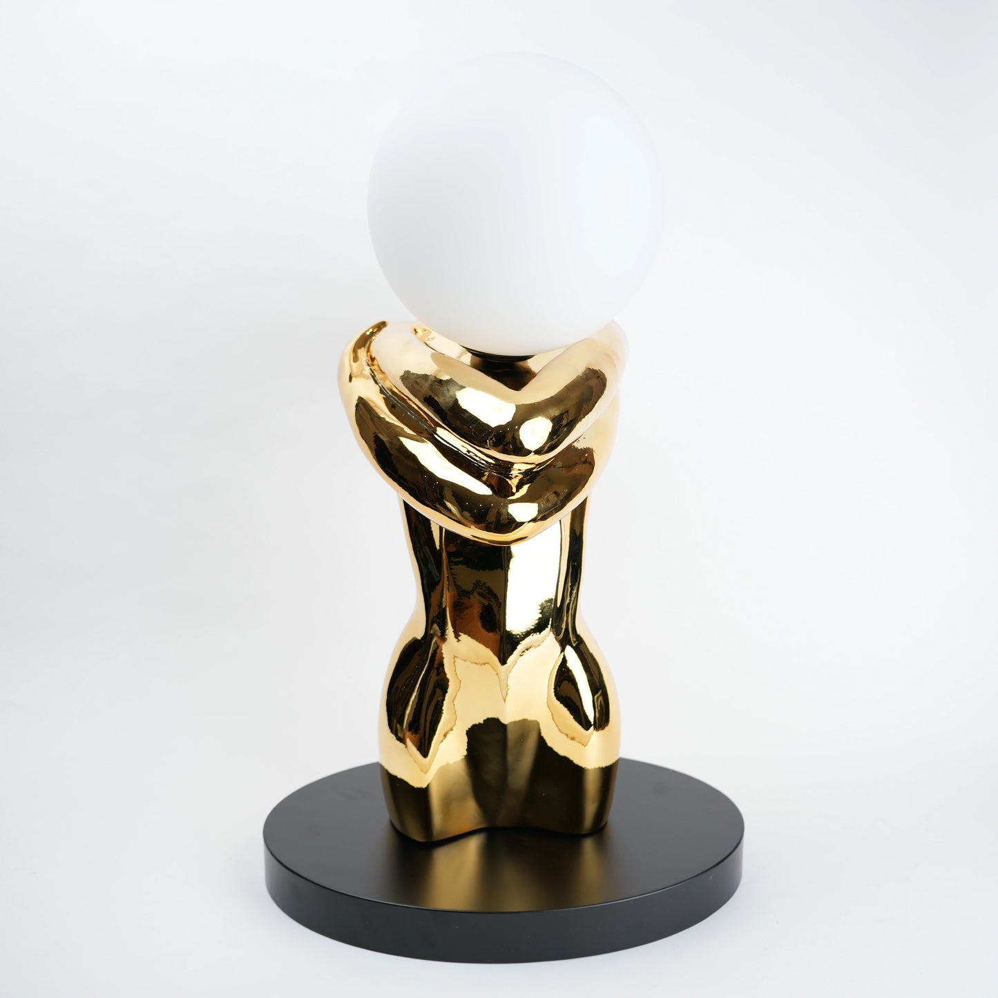 Gold abstract sculpture with a white sphere on a black base against a white background