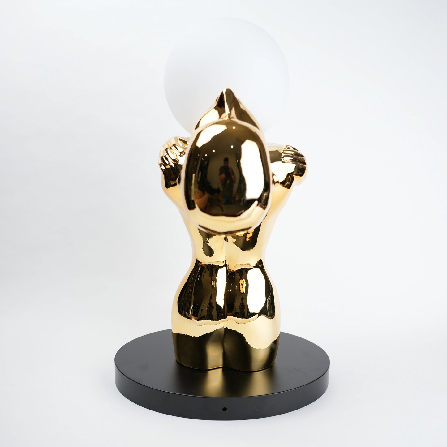 Gold-colored sculpture on a black base against a white background