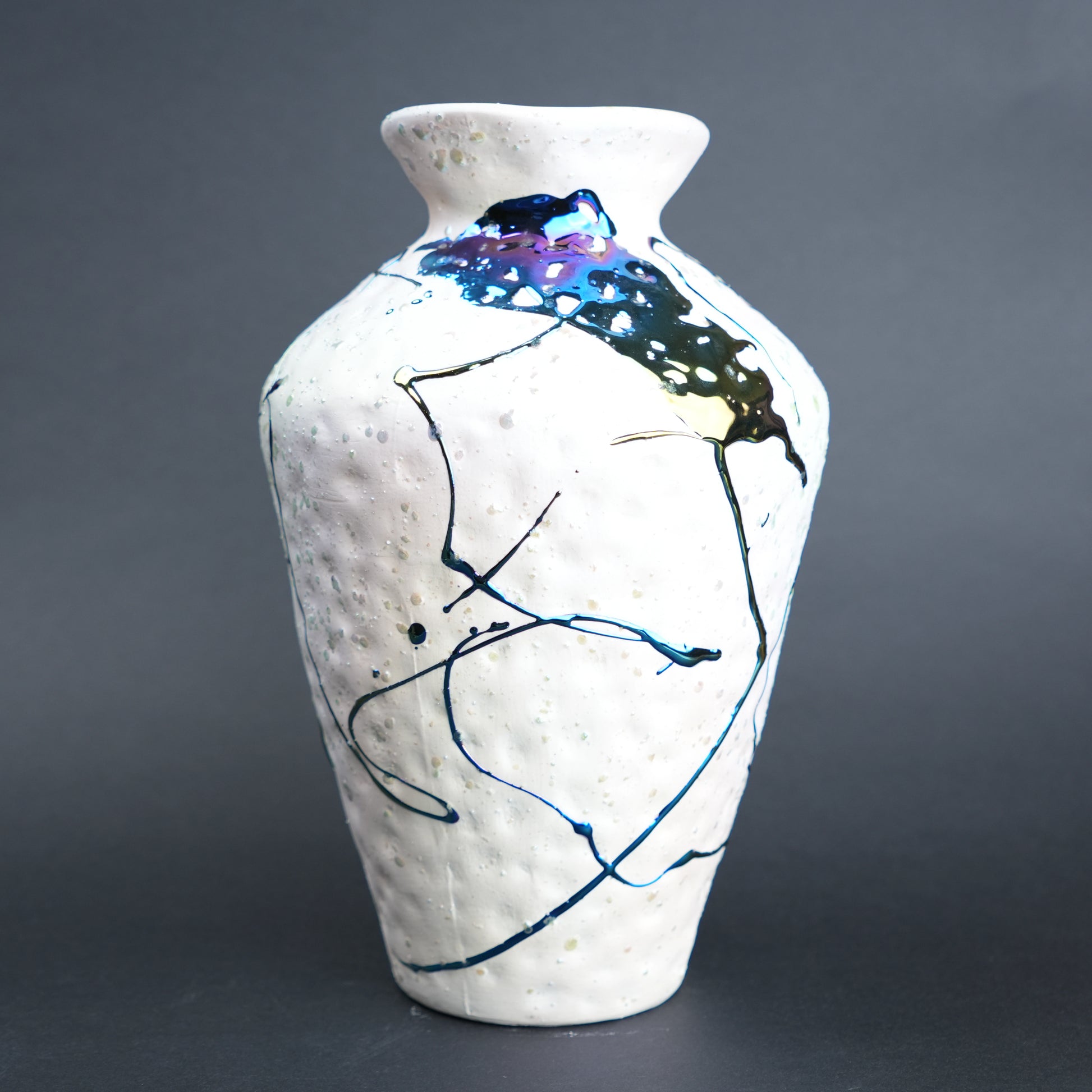 White ceramic vase with abstract black and blue designs on a gray background