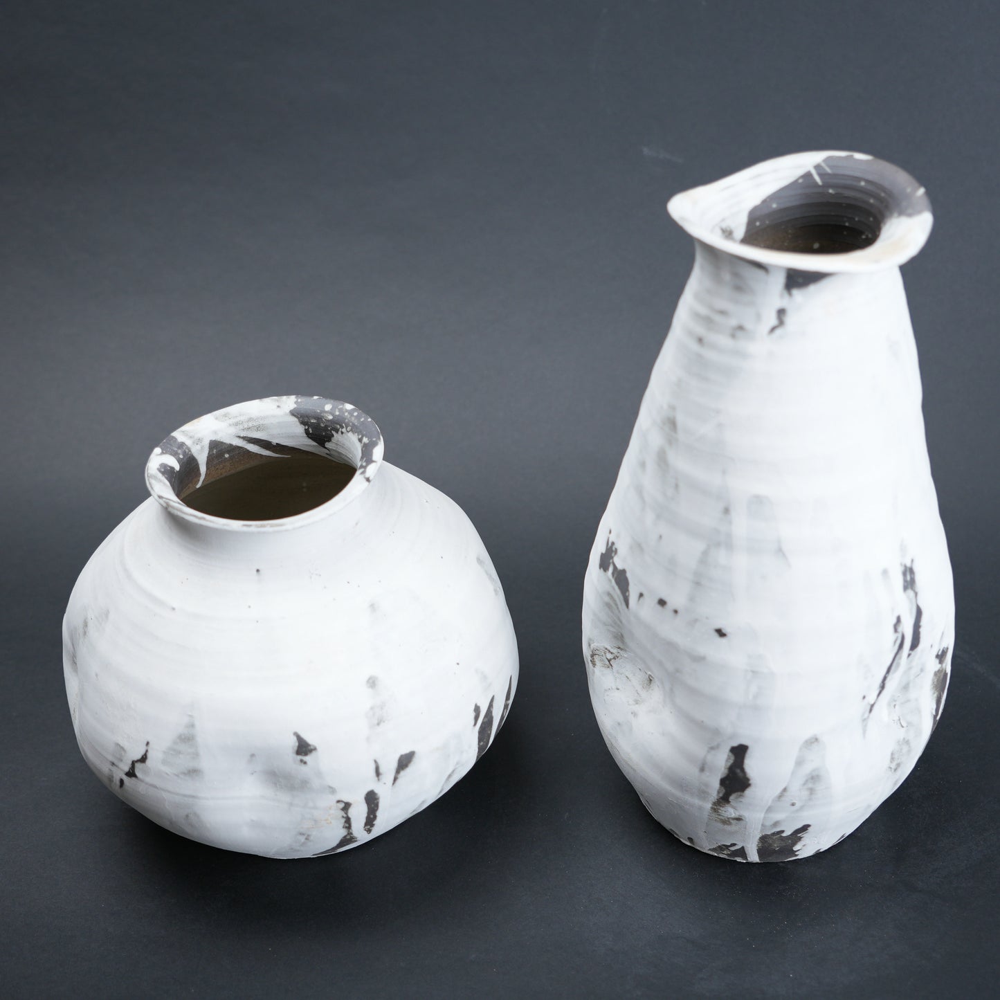 Two white ceramic vases with black speckles on a dark gray background
