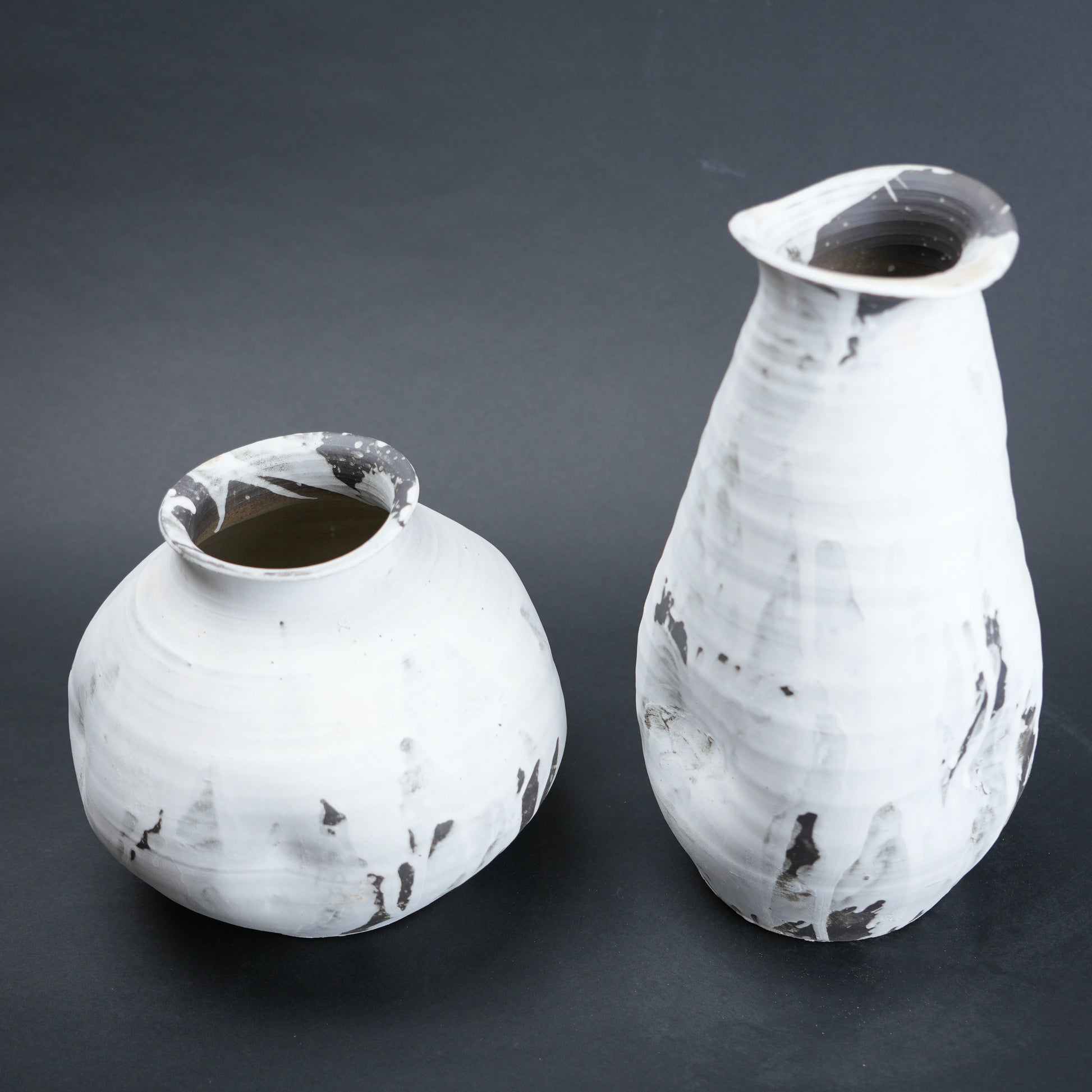 Two white ceramic vases with black speckles on a dark gray background