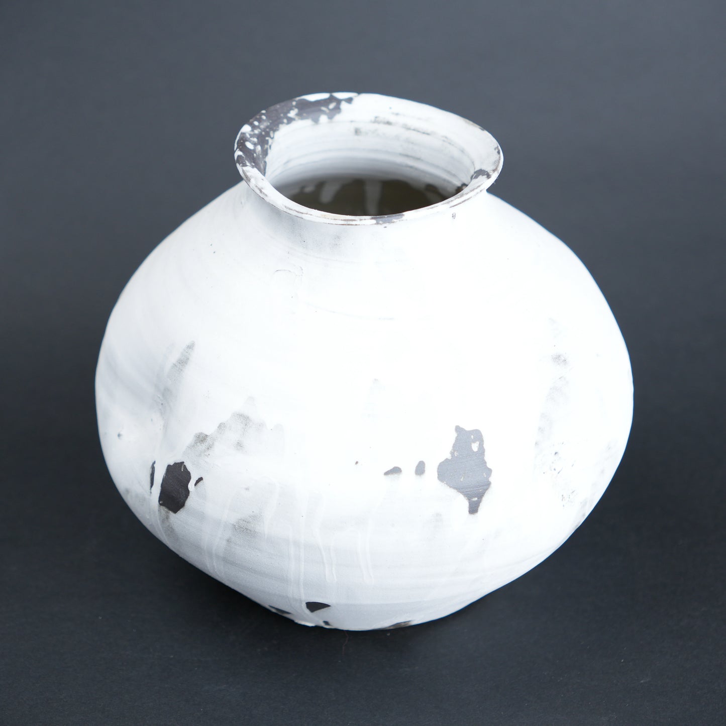 White ceramic vase with black speckles on a dark gray background
