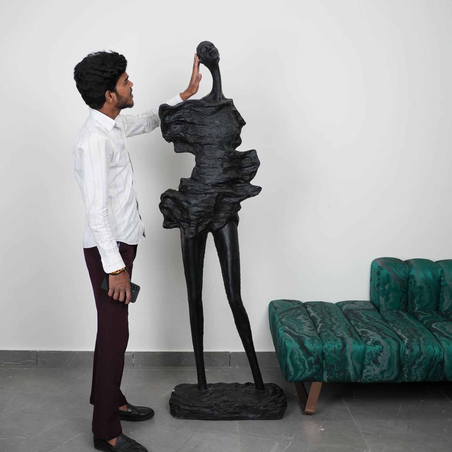 Man interacting with a large black sculpture in a room with a green sofa.