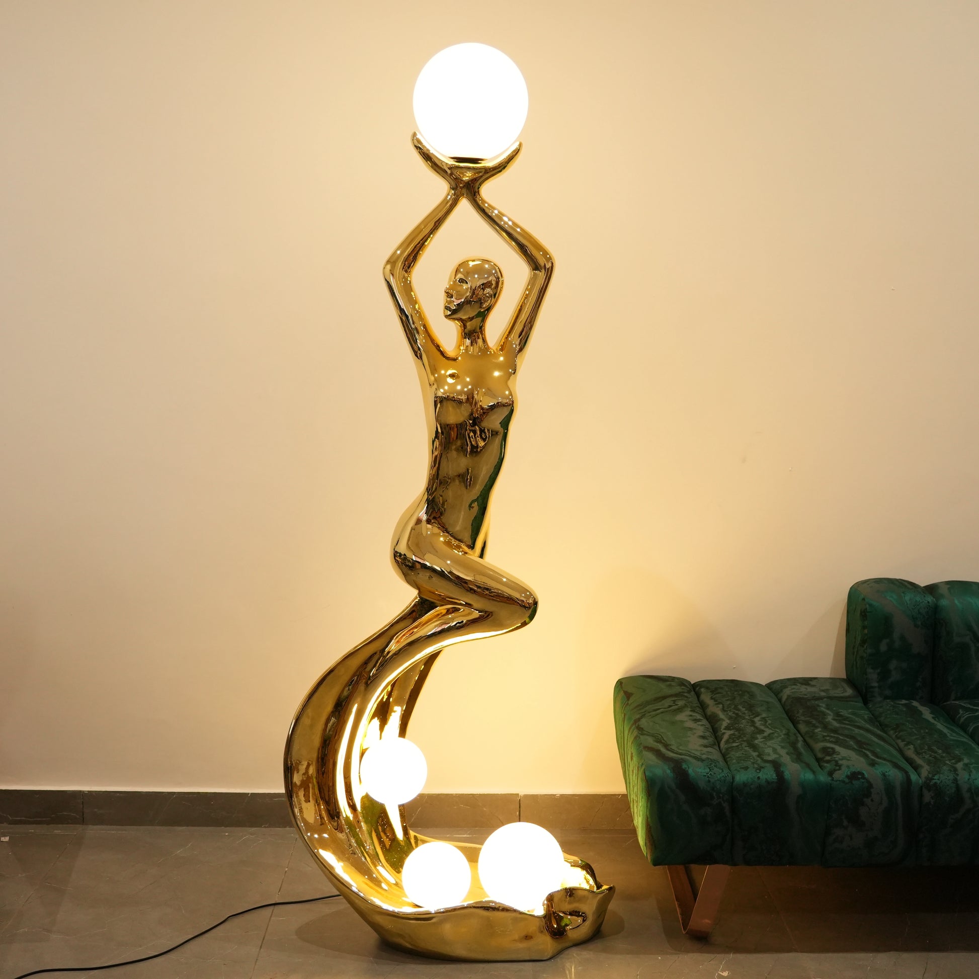 Gold floor lamp shaped like a woman holding a light bulb in a room with a green sofa.