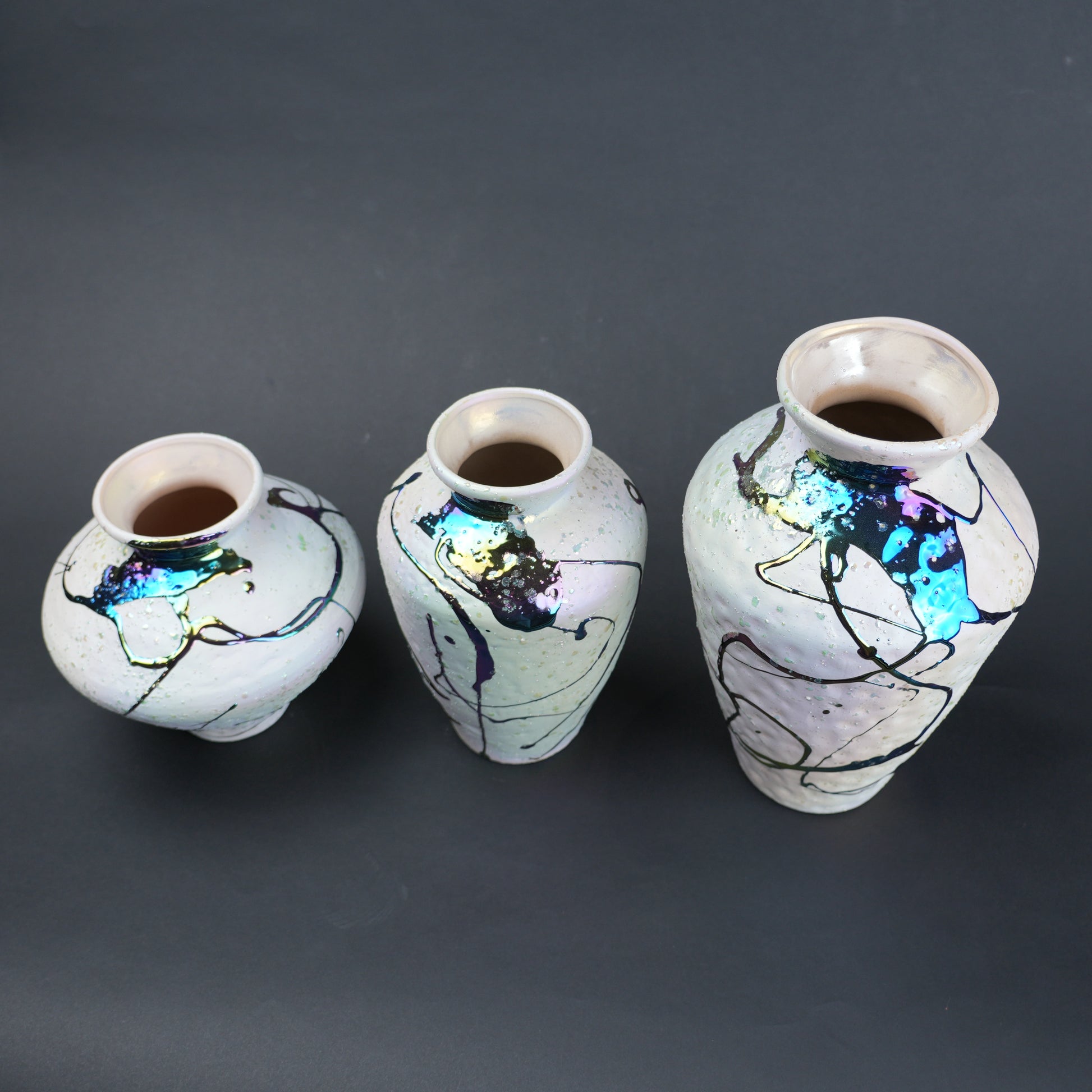 Three ceramic vases with abstract designs on a dark background