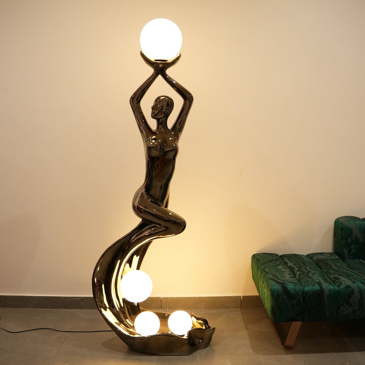 Decorative floor lamp shaped like a woman holding a light bulb in a room with a green sofa.